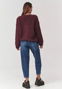 Burgundowy, puszysty sweter o luźnym kroju, zestawiony z niebieskimi spodniami wysokiego stanu i czarnymi trampkami na platformie. Widoczny teksturowany, miękki materiał.