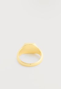 Απλό στιλβωμένο χρυσό δαχτυλίδι σήμα με επίπεδη κορυφή, τοποθετημένο σε λευκή απλή επιφάνεια.