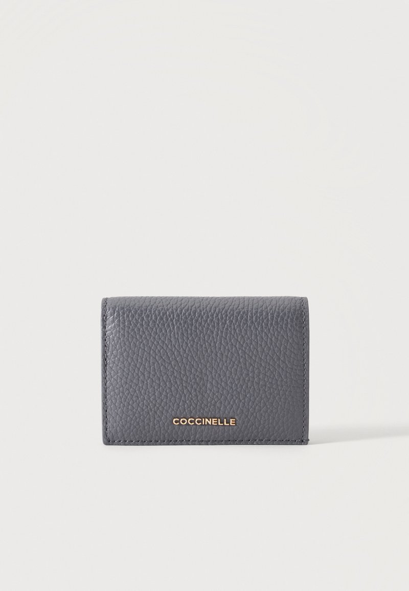 Porte-cartes en cuir texturé gris avec logo COCCINELLE doré centré sur le devant sur fond blanc.