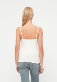 Weißes, geripptes Camisole mit dünnen verstellbaren Trägern und Spitzenbesatz am Ausschnitt, kombiniert mit hellblauen Jeans. Glatte Textur.