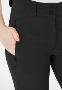 Zwarte, aansluitende broek van rekbaar materiaal, met een gladde textuur, twee knoopsluitingen en een zijzak met rits en logo-detail.