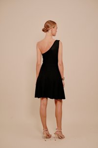 Crna haljina na jedno rame, uski korzet, suknja koja se širi, mekane teksture, dužine iznad koljena, s laganim sjajem. Nošena uz sandale s remenčićima.