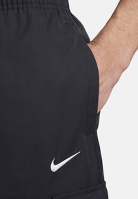Černé sportovní šortky vyrobené z lehkého materiálu s hladkým povrchem, obsahující boční kapsu a bílé logo Nike na levé straně.