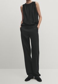 Sort ærmeløs top parret med løstsiddende sorte bukser med en glat tekstur. Sættet suppleres af sorte sko med spids tå.