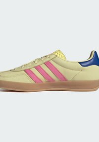 Svijetložuti tenisice s tri ružičaste pruge, svijetlosmeđim gumene potplate i plavim akcentom na peti. Imaju glatku kožu i teksturiran žuti jezik.