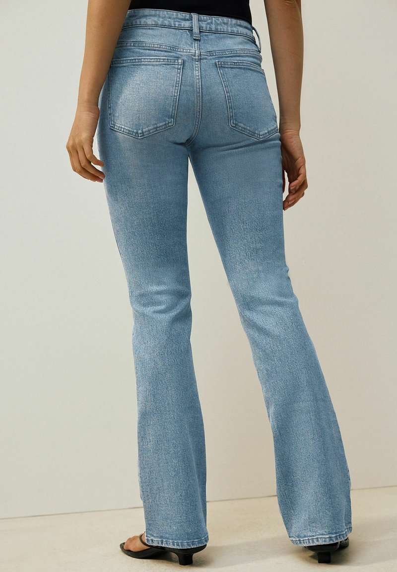 Ljust blå denim jeans med utsvängd byxben, välskräddad midjeband, femficksdesign och subtil textur; lätt sliten look på tyget.