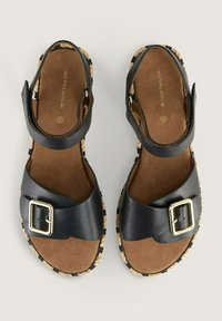 Black leather sandals with a wide strap and gold buckle on a cork sole, featuring braided accents around the edge. Flat design.