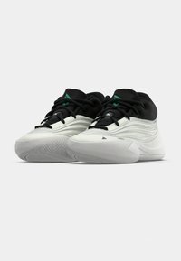 Par tenisica u crnoj i bijeloj boji za sport s teksturiranim potplatima, crnim vezicama i zelenim trokutastim logotipima na jeziku, nagnute jedna pored druge.