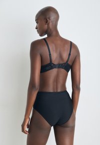 Zwarte kanten bralette met verstelbare bandjes, mesh-details en een haak-en-oogsluiting. Hoge zwarte slip met een gladde textuur.