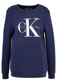 Mörkblå sweatshirt i bomull med rund halsringning. Har en stor vit "CK"-logotyp och texten "Calvin Klein Jeans" på framsidan.
