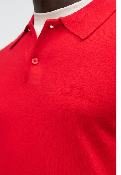 Camisa polo vermelha com colarinho, pala de dois botões e um tecido texturizado. Detalhe discreto do logótipo na mesma cor no peito.