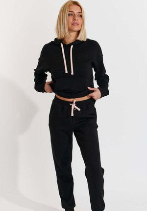 Felpa nera corta con tasca frontale e cappucci a contrasto, abbinata a pantaloni jogger neri con stringhe coordinate.
