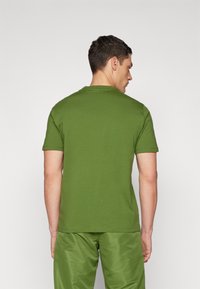 Zöld crew neck póló, hátulról nézve, rövid ujjú, pamutból készült, sima textúrájú, egyenes szabású és minimalista díszítéssel.
