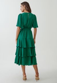 Green, layered maxi dress with short sleeves, a fitted waist, and a back button closure, made from a lightweight fabric.