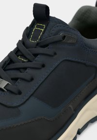 Tumesinine sneaker sileda, mati viimistlusega. Omab kihilist tekstuuri, ümmargust varvast, kontrastseid õmblusi ja kummist tallat.