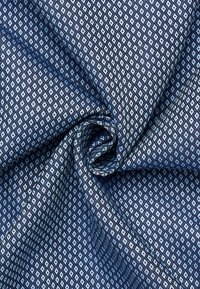 Tessuto blu attorcigliato per formare un nodo, caratterizzato da un motivo a piccole diamanti ripetitivo in tonalità di blu scuro e chiaro.