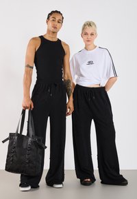 Black sleeveless tank top, black loose-fit pants with star patterns, and a black tote bag; white T-shirt with logo, black accents.