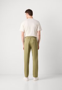Beige t-shirt för män med korta ärmar, i kombination med olivgröna byxor med elastisk midja och en bakficka.
