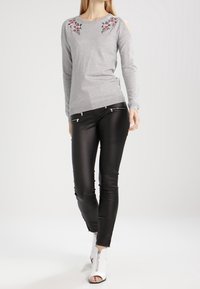 Ljusgrå tröja med blommig broderi vid axlarna, kombinerad med tighta svarta faux läderbyxor med dragkedjeaccentuer. Skorna är vita öppna stövlar.