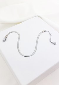 Srebrny wężykowy bransoletka z zapięciem i regulowaną długością. Posiada gładką teksturę i subtelny blask, prezentowana w białym pudełku.