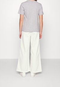 Camiseta de algodón gris combinada con pantalones anchos blancos, con un corte relajado y un diseño sencillo. Los pantalones tienen una superficie ligeramente texturizada.