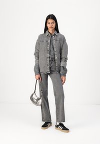Veste en denim grise sur un pull et un pantalon gris assortis, accompagnée de baskets noires avec des rayures blanches et d'un sac à main argenté.