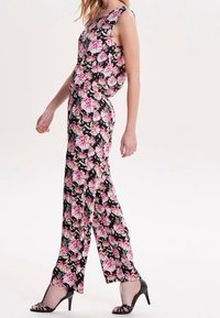 Mono floral con fondo negro, que presenta patrones en rosa y verde. Diseño sin mangas con piernas anchas y un ajuste relajado.