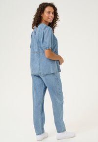 Îmbrăcăminte din denim de un albastru deschis, care include un top cu mâneci scurte și bufante, împreună cu pantaloni largi asortați. Detalii simple de cusătură pe tot parcursul.