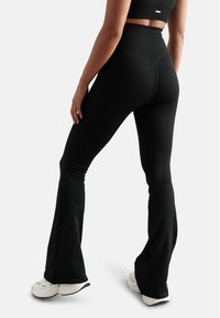 Schwarze, gerippte, ausgestellte Hosen mit hohem Bund, strukturiertem Stoff und einer figurbetonten Silhouette. Tragen Sie sie mit weißen Sneakers.