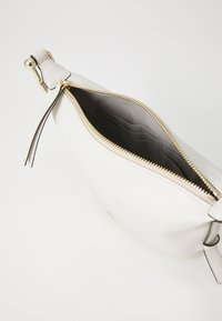 Borsa a tracolla bianca in pelle con chiusura a zip e hardware dorato, dotata di un interno con più scomparti per carte e un rivestimento testurizzato.