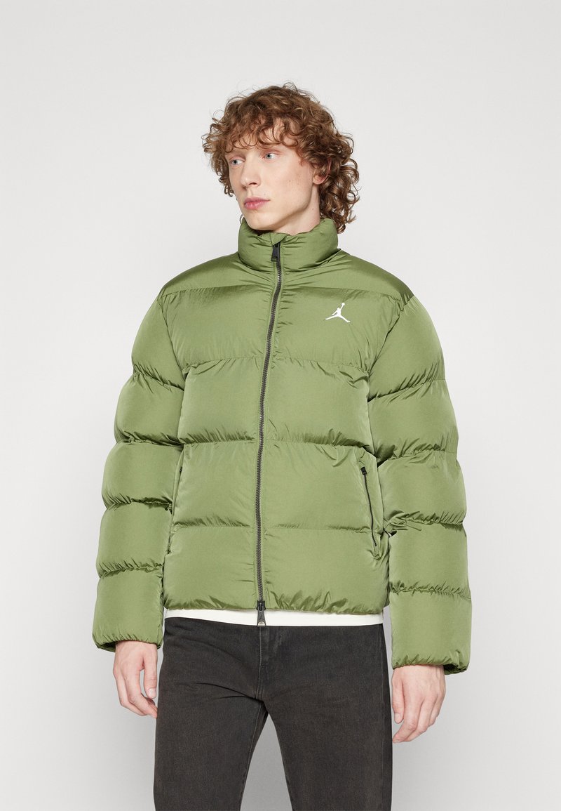 Giacca imbottita color verde oliva con colletto alto, chiusura con zip e motivo a quadri. Presenta un logo bianco sul petto sinistro e tasche laterali.