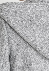 Grå ullblandad kappa med en texturerad, mjuk yta och en bred krage. Designen har strukturerade sömmar och en modern silhuett.