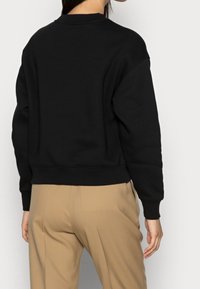 Felpa nera cropped con spalle scese, polsini e orlo a coste; abbinata a pantaloni beige. Tessuto morbido e liscio.