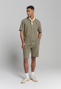 Olijfgroen bijpassende korteknopen-overhemd met korte mouwen en korte broek set, met een relaxte pasvorm, een kraag en een lichte sjaal als accessoire.