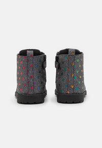 Botines negros hasta el tobillo con un acabado brillante, decorados con patrones de corazones coloridos, tela texturizada y suela resistente. Vista trasera que muestra detalle de hebilla.