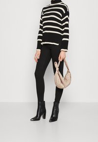 Pull en maille rayé noir et blanc, leggings noirs ajustés, bottines en cuir noires et un sac à main beige doux avec poignée nouée.