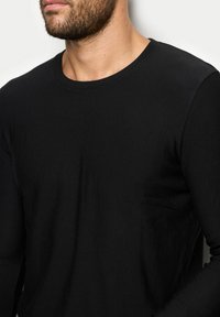 Czarna koszulka z długim rękawem o okrągłym dekolcie i slim fit, wykonana z miękkiej, elastycznej mieszanki bawełny; posiada subtelną kieszeń na bocznym szwie.