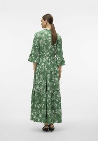 Grön lång klänning med vitt blommönster, volangärmar, lagerdesign och bältesmidja. Materialet verkar slät och lätt.