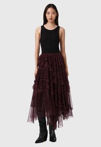 Top preto sem mangas combinado com uma saia longa, em burguês, de camadas com babados, feita de tule. Botas de salto alto, pretas, até ao joelho completam o look.