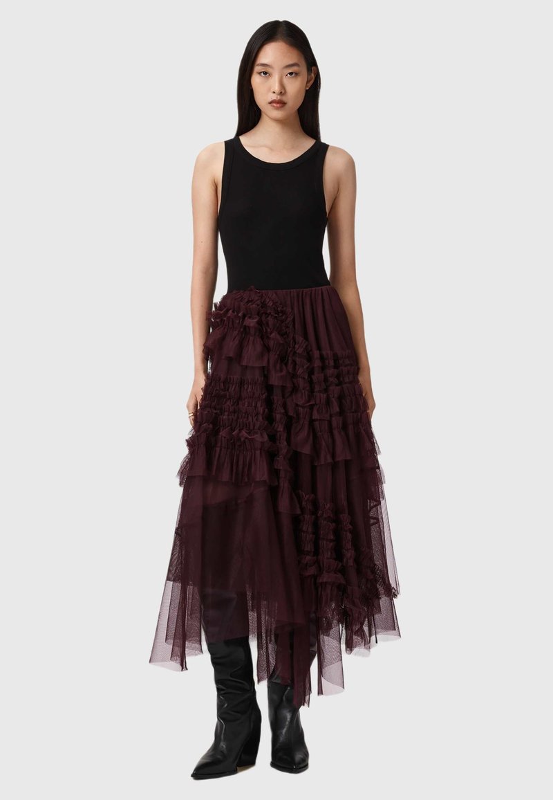 Top preto sem mangas combinado com uma saia longa, em burguês, de camadas com babados, feita de tule. Botas de salto alto, pretas, até ao joelho completam o look.