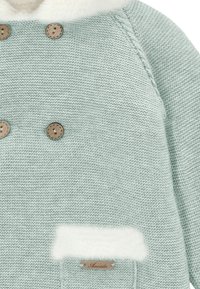 Cárdigan de punto en verde menta pálido, con tejido texturizado, cuatro botones marrones y un detalle de bolsillo de pelo sintético blanco con una etiqueta de madera.