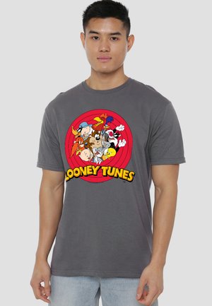 Young man wearing gray t-shirt with colorful Looney Tunes characters clustered inside a red target circle and yellow text below.