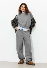 Sweatshirt gris et pantalon de survêtement assorti en tissu doux, superposé sur une chemise bleu clair. Veste en cuir marron et chaussures à imprimé animal complètent le look.