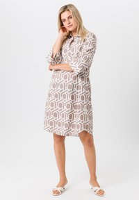 Robe A-line à manches courtes en beige avec un motif géométrique blanc, un col et une fermeture à boutons, fabriquée dans un tissu léger.
