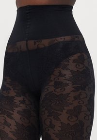 Høytlivede svarte shaping tights med et gjennomskinnelig blomsterlacemønster, glatt midjebånd og en ugjennomsiktig svart del på toppen.