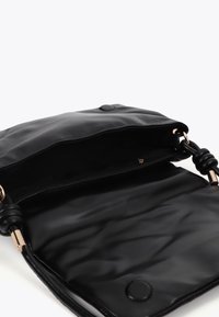 Svart läder crossbody-väska med en slät textur, som har en dragkedjeficka med guldhardware och en cirkelknappdetalj på framsidan.