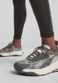 Chaussures de sport grises et noires avec un dessus texturé, des matériaux contrastants et des accents en jaune fluo. Caractéristiques d'un design à lacets et d'une semelle rembourrée.