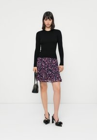 Μαύρη μπλούζα με μακριά μανίκια και ραφές συνδυασμένη με μια ροή φούστα σε μωβ floral μοτίβο. Το μοντέλο κρατά μια μικρή μαύρη τσάντα και φοράει μαύρες γόβες.