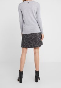 Vaaleanharmaa pitkähihainen villapaita, jossa on ribbikudos, yhdistetty musta-valkoraidalliseen hameeseen. Asua täydentävät mustat neliökorot ankle boots -kengät.