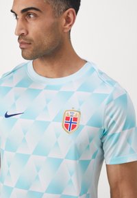 Hele sinine spordisärk geomeetrilise mustriga, rinnal kollane, punane ja sinine vapp ning vasakul tumesinine Nike logo.